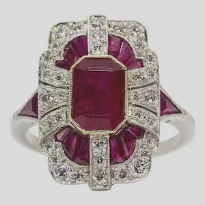 Peut inclure: Bague en argent ornée d'un grand rubis rectangulaire, entouré de petits rubis et diamants. La bague présente un style Art Déco, avec un design symétrique et une bordure dorée autour du rubis central.