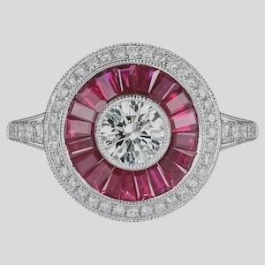 Peut inclure: Bague en platine ornée d'un diamant central rond entouré de pierres rouges et de petits diamants. La monture de la bague est également sertie de diamants, créant un design luxueux et élégant. Le design est de style Art Déco.