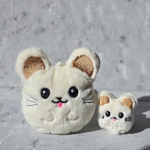 May include: Two plush mouse toys. The larger mouse is off-white with gold-colored inner ears, black eyes, and a pink tongue. The smaller mouse has the same features. Both have embroidered whiskers and a cute expression.