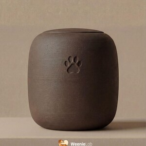 May include: A brown ceramic pet urn with a paw print design. The urn has a rounded shape with a lid and is displayed on a neutral surface. The WeenieLab logo is visible in the bottom right corner.