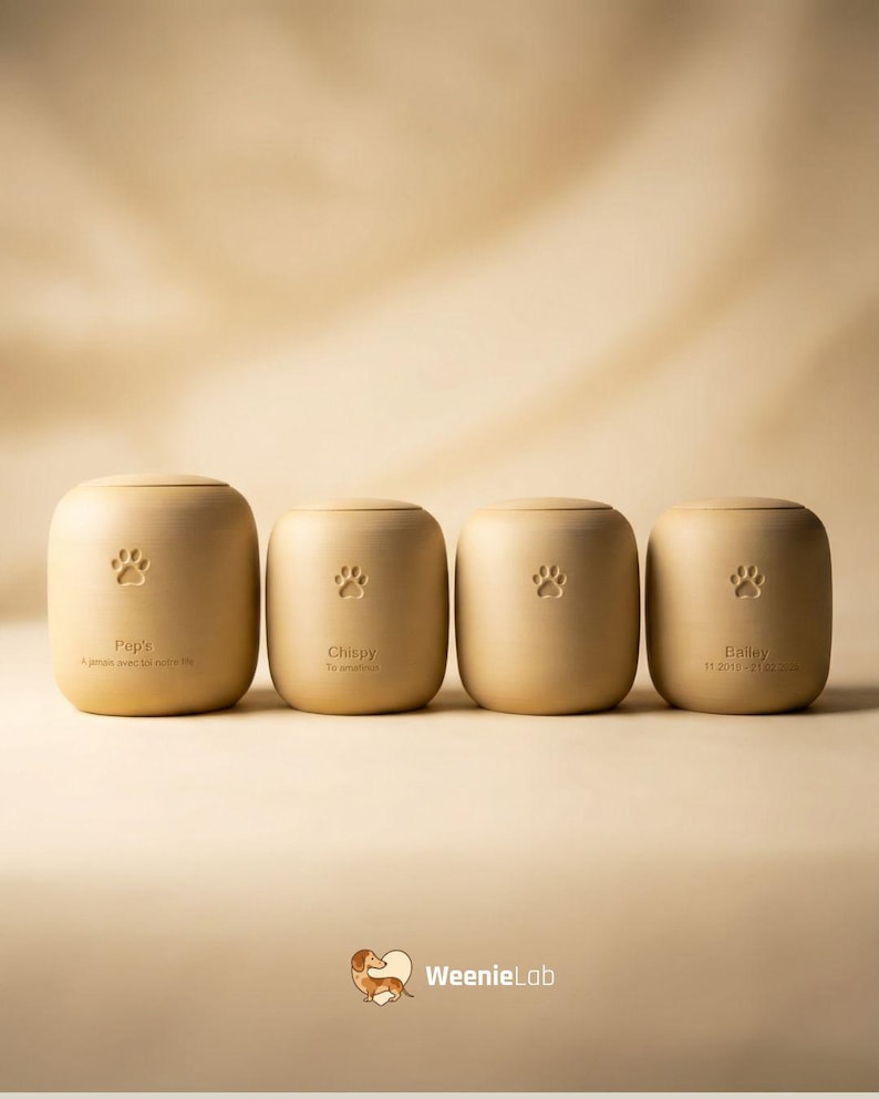 May include: Four beige pet urns with paw print designs. Each urn has a name and date engraved. The urns are arranged in a row against a neutral background. The WeenieLab logo is at the bottom.