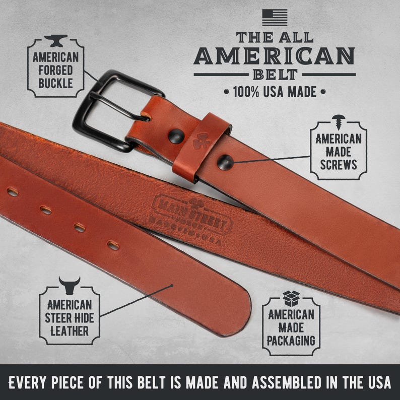 Op de afbeelding: Een close-up van een bruine leren riem met een zwarte gesp. De riem is gelabeld "The All American Belt" en "100% USA Made". De afbeelding benadrukt kenmerken zoals een Amerikaanse gesmede gesp, rundleer en in Amerika gemaakte schroeven en verpakking.