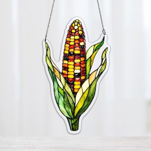 May include: A stained glass corn decoration with a chain for hanging. The corn features kernels in shades of yellow, red, and orange, surrounded by green and yellow leaves. The artwork is designed to resemble a realistic ear of corn.