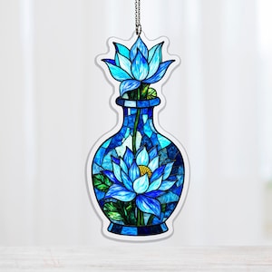 Könnte beinhalten: Blaues Ornament im Stil eines Glasfensters mit einer Vase mit zwei blauen Lotusblumen. Die Vase ist ein Mosaik aus Blautönen mit weißer Umrandung. Das Ornament hängt an einer silbernen Kette, geeignet für ein Fenster oder einen Rückspiegel.