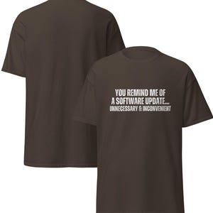 May include: A brown t-shirt with the text "YOU REMIND ME OF A SOFTWARE UPDATE... UNNECESSARY & INCONVENIENT" in white. Another brown t-shirt is visible behind the first.