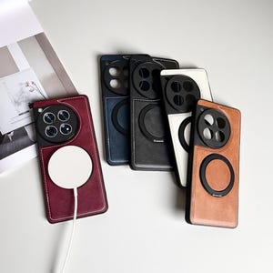 Puede incluir: Una colección de fundas de teléfono de cuero en varios colores: burdeos, azul marino, negro, blanco y marrón claro. Cada funda presenta un recorte circular para la cámara y un anillo de carga magnético. Costuras blancas y cable de carga blanco.