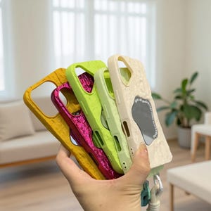 May include: A collection of colorful phone cases in shades of yellow, magenta, green, and off-white. The cases have a textured surface and a cutout for the camera. Some cases have a reflective surface.