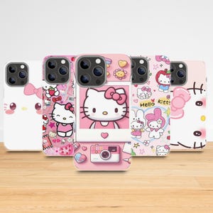 May include: A collection of five phone cases featuring Hello Kitty designs. The cases are primarily pink and white, with various illustrations of Hello Kitty, bows, strawberries, and other cute elements. The cases are displayed on a light brown wooden surface.