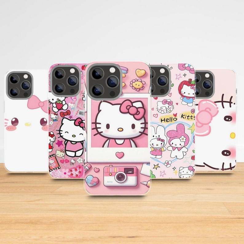 May include: A collection of five phone cases featuring Hello Kitty designs. The cases are primarily pink and white, with various illustrations of Hello Kitty, bows, strawberries, and other cute elements. The cases are displayed on a light brown wooden surface.