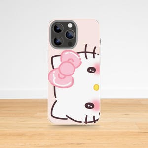 May include: A pink phone case featuring a cartoon illustration of a cat with a pink bow, black eyes, and a yellow nose. The case has a light pink background and a glossy finish.