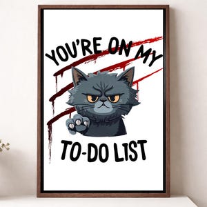 Könnte beinhalten: Gerahmtes Kunstwerk mit einer grimmigen grauen Katze mit gelben Augen und erhobener Pfote. Der Text "YOU'RE ON MY TO-DO LIST" ist in Schwarz dargestellt, mit roten Streifen hinter der Katze, was ein humorvolles und kantiges Design ergibt.