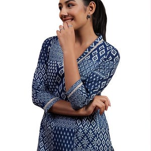 May include: A navy blue tunic with a white geometric pattern. The tunic has a V-neckline and three-quarter sleeves, trimmed with white and gold accents. The fabric has a textured appearance.