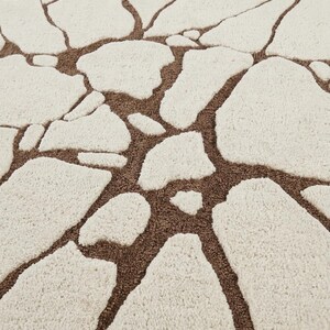 May include: A tufted area rug featuring a high-pile cream-coloured pattern of irregular, stone-like shapes separated by recessed, low-pile brown channels that create a textured, mosaic-inspired design across the entire surface of the textile.