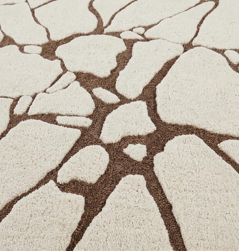 May include: A tufted area rug featuring a high-pile cream-coloured pattern of irregular, stone-like shapes separated by recessed, low-pile brown channels that create a textured, mosaic-inspired design across the entire surface of the textile.
