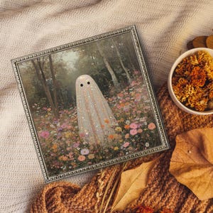 May include: A framed art print featuring a whimsical ghost in a field of colorful flowers. The ghost is white with black eyes and glitter accents. The frame is silver with a decorative border. A bowl of dried flowers and a fall leaf are also visible.