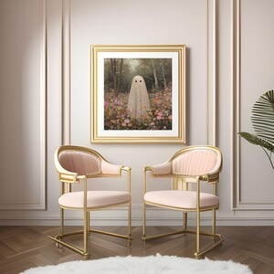 May include: A framed art print featuring a ghost figure in a field of flowers. The artwork is in a gold frame, hanging above two pink and gold chairs. The chairs have a curved back and armrests, with a plush seat. A white rug is on the floor.