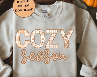 May include: Cream-colored sweatshirt with the words "COZY Season" in a fall-themed design. The word "COZY" features pumpkin and plaid patterns, while "Season" is in a script font. The image also includes the text "INSTANT DIGITAL DOWNLOAD".