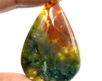 May include: A teardrop-shaped gemstone with a polished surface. The stone features a blend of colors, including deep greens, rusty reds, and golden yellows. The gemstone is held between fingers, showcasing its natural beauty and unique color patterns.