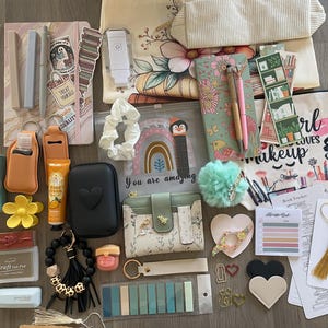 May include: An assortment of stationery and accessories, including notebooks, pens, a wallet, a hand sanitiser holder, a lip balm, a pom-pom, and a tote bag. The items are arranged on a wooden surface, with a variety of colours and textures.