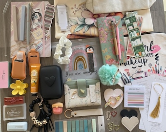 May include: A collection of stationery and accessories, including notebooks, pens, a wallet, a hand sanitizer holder, a lip balm, a pom-pom, and a tote bag. The items are arranged on a wooden surface, with a variety of colors and textures.