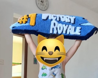 Peut inclure: Un tapis bleu et jaune avec les mots "VICTORY ROYALE" en blanc. Le tapis est tenu par une personne. Le tapis a une bordure bleue et un numéro un jaune.