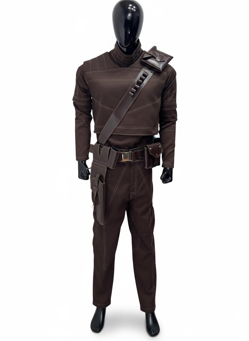 May include: A brown costume with white stitching, displayed on a mannequin. The outfit includes a long-sleeved top, pants, a belt with pouches, and a shoulder strap with a pouch. The mannequin has a black head and hands.