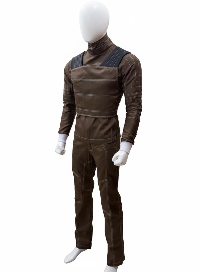 May include: Brown jumpsuit with white stitching details, featuring a high collar and shoulder straps. The long-sleeved top has white cuffs, and the pants have reinforced knee panels. This outfit is displayed on a mannequin.