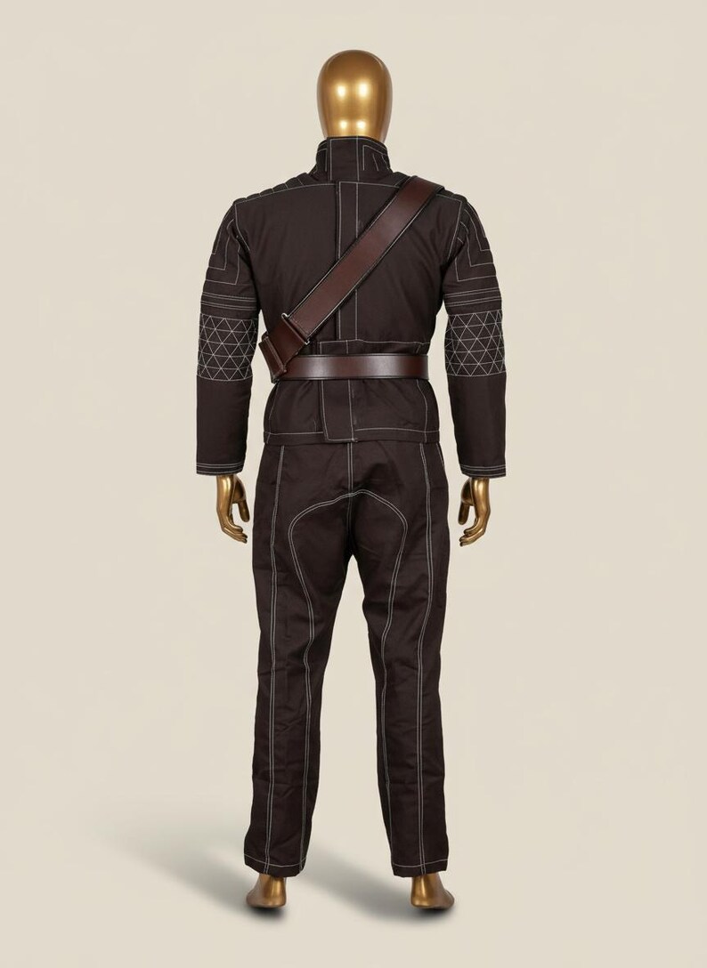 Puede incluir: Mono marr&oacute;n con costuras blancas, bandolera y cintur&oacute;n de cuero marr&oacute;n, expuesto en un maniqu&iacute;. El conjunto presenta un cuello alto y patrones geom&eacute;tricos en las mangas. El maniqu&iacute; tiene cabeza y manos doradas.