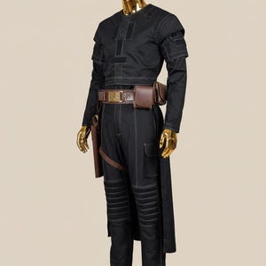 May include: Black costume with white stitching, featuring a long-sleeved top, cargo pants, and a long coat. The outfit includes a brown belt with pouches and a holster. The mannequin has a gold head, hands, and feet.