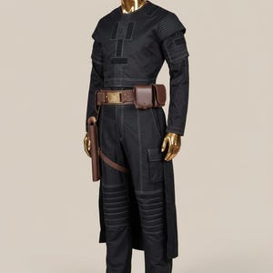 May include: Black costume with white stitching, displayed on a gold mannequin. The outfit includes a long-sleeved top, pants, and a belt with pouches. A holster is attached to the belt. The costume has a futuristic or sci-fi aesthetic.