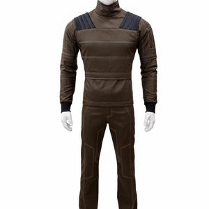 May include: A brown jumpsuit displayed on a mannequin. The long-sleeved top has a high collar and horizontal stitching. The shoulders have black padded accents. The pants have reinforced stitching around the knees and pockets. The jumpsuit is made of a durable material.
