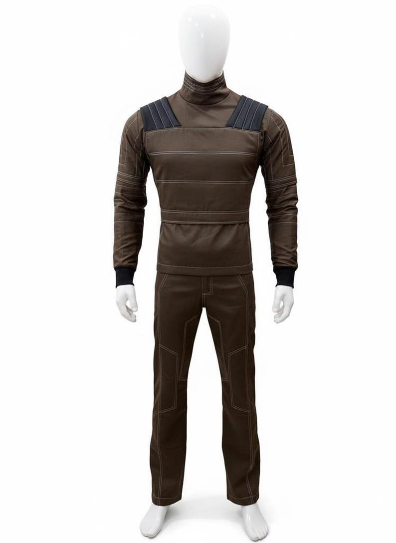 May include: A brown jumpsuit displayed on a mannequin. The long-sleeved top has a high collar and horizontal stitching. The shoulders have black padded accents. The pants have reinforced stitching around the knees and pockets. The jumpsuit is made of a durable material.