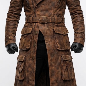 May include: Brown leather trench coat with multiple pockets, a belt, and a zipper closure. The coat has a distressed finish and is worn with black gloves. A stylish outerwear garment.