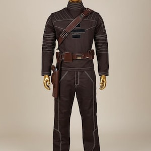 Puede incluir: Un mono marr&oacute;n con costuras blancas, cuello alto y cintur&oacute;n y funda de cuero marr&oacute;n. El atuendo se exhibe en un maniqu&iacute; con cabeza y manos doradas. El mono tiene una correa para el hombro y un cintur&oacute;n con hebilla plateada.