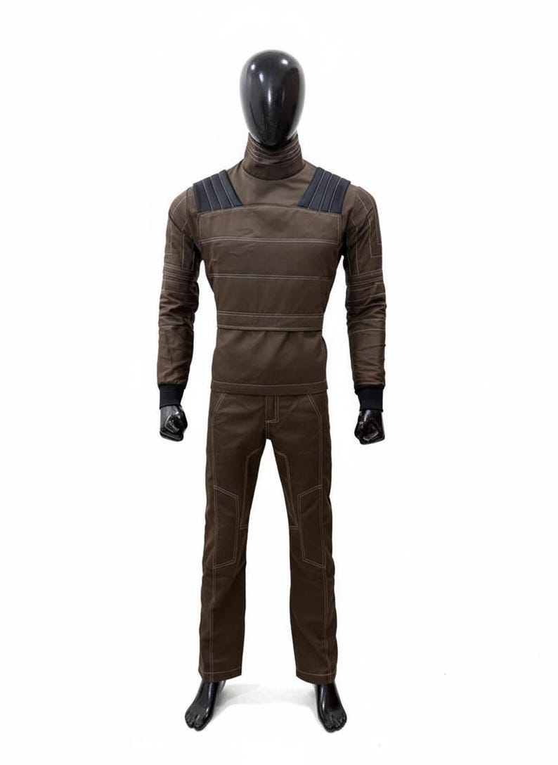 May include: A brown jumpsuit displayed on a mannequin. The outfit includes a long-sleeved top with a high collar and horizontal stitching, and matching pants. The shoulders have dark gray accents, and the cuffs are black.