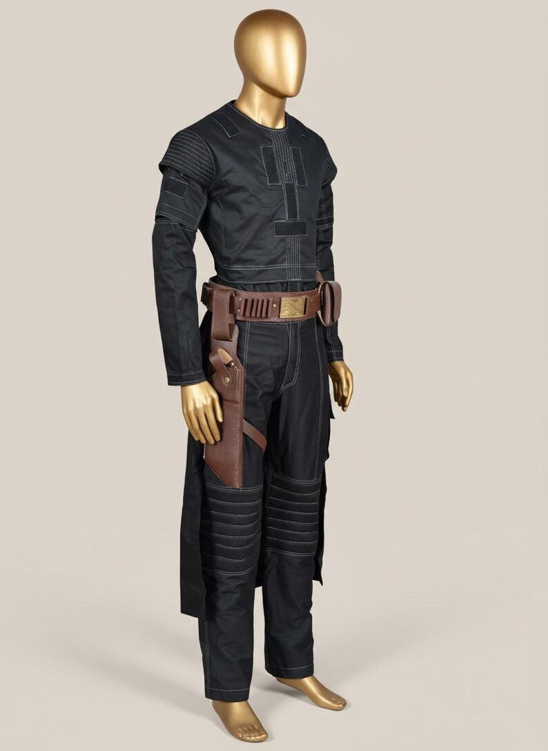 May include: Black costume with white stitching, displayed on a mannequin. The outfit includes a long-sleeved top, pants, and a brown leather belt with a holster. The pants have padded knee details. The mannequin has a gold finish.