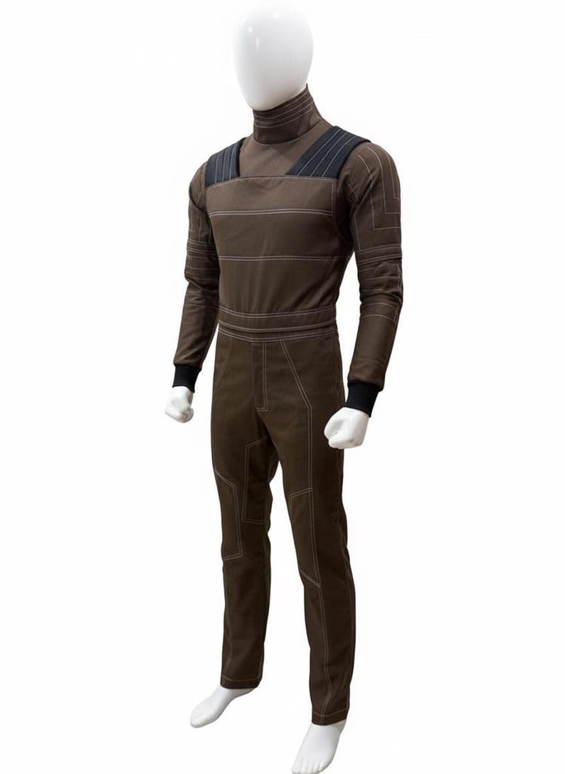 May include: Brown jumpsuit with white stitching details, displayed on a mannequin. The jumpsuit features a high collar, long sleeves with black cuffs, and a tailored fit. The design includes shoulder straps and horizontal stripes across the chest.