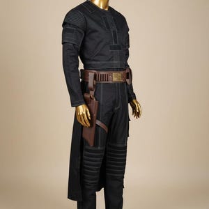 May include: Black costume with white stitching, displayed on a mannequin. The outfit includes a long-sleeved top, pants, and a belt with a holster. The mannequin has a gold-colored head and hands. The costume has a futuristic or sci-fi theme.