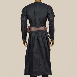 May include: Black costume with white stitching details, displayed on a mannequin. The outfit includes a long coat, pants, and a brown belt with pouches. The mannequin has a gold head.