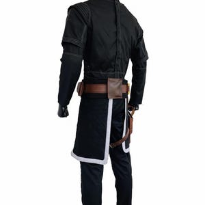 May include: Black costume with white stitching and trim, featuring a jacket, trousers, and a belt with pouches. The costume includes a quilted skirt-like piece with white trim. The mannequin has a gold head.
