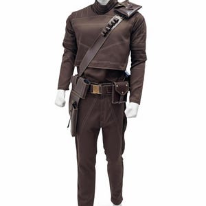 May include: Brown costume with a high collar, long sleeves, and matching pants. The outfit features white stitching details, a shoulder strap with pouches, and a belt with a gold buckle. Additional pouches are attached to the belt and leg.