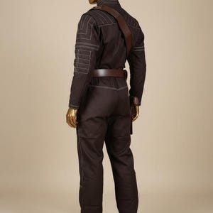 Puede incluir: Mono marr&oacute;n con detalles de costuras blancas, cintur&oacute;n marr&oacute;n y correa para el hombro marr&oacute;n. El mono tiene bolsillos en las mangas y las piernas. El maniqu&iacute; tiene cabeza y manos doradas.