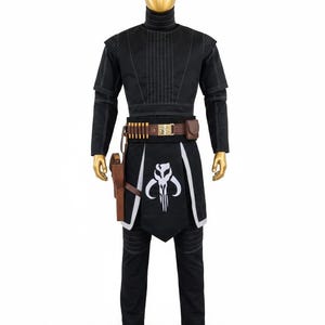 May include: Black costume with white detailing, comprising a high-necked top, trousers, and a decorative apron with a white skull emblem. Includes a brown belt with pouches and a holster. The mannequin is gold.