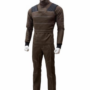 May include: Brown jumpsuit with a high collar, long sleeves, and matching pants. The outfit features white stitching details and black accents on the shoulders and cuffs. The mannequin is wearing a brown outfit.