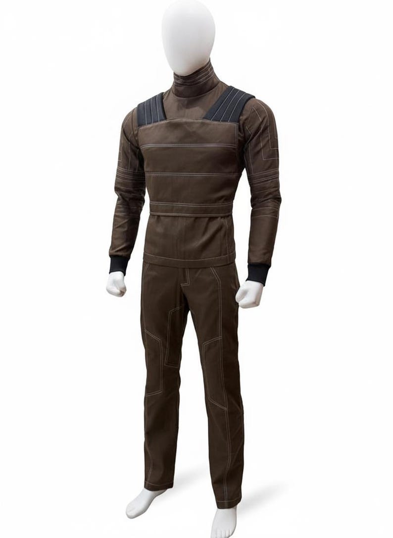 May include: Brown jumpsuit with a high collar, long sleeves, and matching pants. The outfit features white stitching details and black accents on the shoulders and cuffs. The mannequin is wearing a brown outfit.