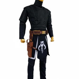 May include: A black costume with a high collar, featuring a brown belt with ammunition and a holster. The costume includes a black and white skirt with a skull emblem and black trousers. The mannequin has a gold head and feet.