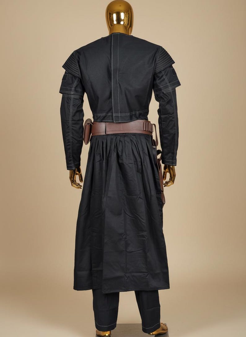 May include: Black costume with a long coat, pants, and a brown belt with pouches. The costume has white stitching details and is displayed on a gold mannequin. The outfit is reminiscent of a sci-fi or fantasy character.