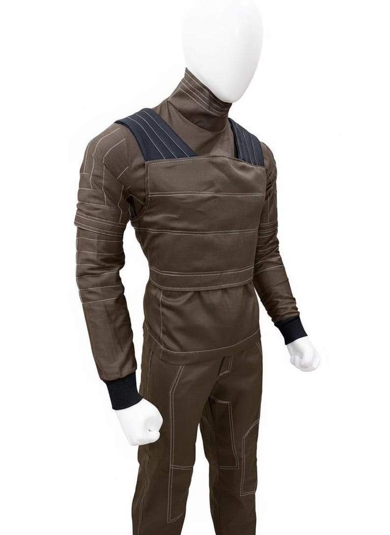 May include: Brown jumpsuit with a high collar and long sleeves, displayed on a mannequin. The suit features white stitching details and black accents on the shoulders and cuffs. The overall design suggests a utilitarian or workwear aesthetic.