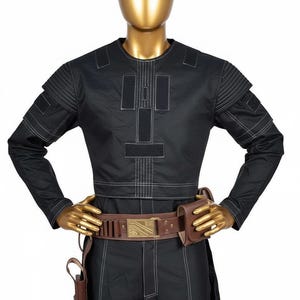 May include: Black jumpsuit with white stitching, featuring a round neck and long sleeves. The costume includes a brown belt with a gold buckle, a holster, and a pouch. The outfit is displayed on a gold mannequin.