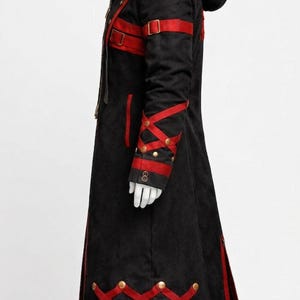 May include: Black hooded coat with red accents. The long coat features red straps, gold-colored buttons, and decorative red trim. The sleeves have a crisscross design with gold buttons. The coat is displayed on a mannequin.